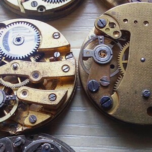 May include: Close-up of several antique watch movements, showcasing intricate gears, screws, and metal components. The watch parts are in various stages of disassembly, revealing the internal mechanisms. The brass and silver-colored elements are visible.