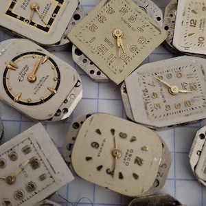 May include: A collection of vintage watch faces with various shapes and designs. The faces are primarily white or cream-colored, with gold-toned hands and numerals. Some have visible brand names and markings, showcasing a variety of styles.