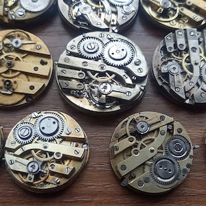 May include: A collection of vintage watch movements, showcasing intricate gears, springs, and other mechanical components. The movements are circular, with brass and silver-colored metal elements. The image highlights the detailed craftsmanship of antique timepieces.