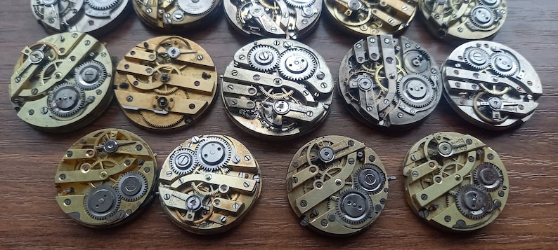 May include: A collection of vintage watch movements, showcasing intricate gears, springs, and other mechanical components. The movements are circular, with brass and silver-colored metal elements. The image highlights the detailed craftsmanship of antique timepieces.