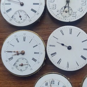 May include: A collection of vintage watch faces with white dials and black Roman numeral hour markers. Some faces have sub-dials and delicate hands. One face is marked "ETERNA", and another reads "UNION HORLOGERE".