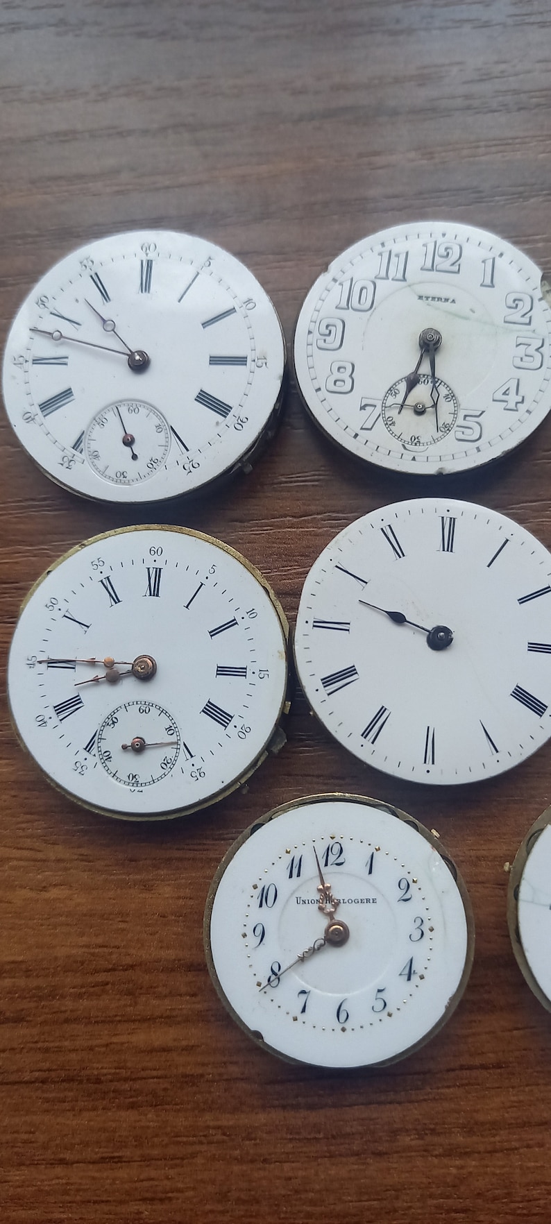 May include: A collection of vintage watch faces with white dials and black Roman numeral hour markers. Some faces have sub-dials and delicate hands. One face is marked "ETERNA", and another reads "UNION HORLOGERE".