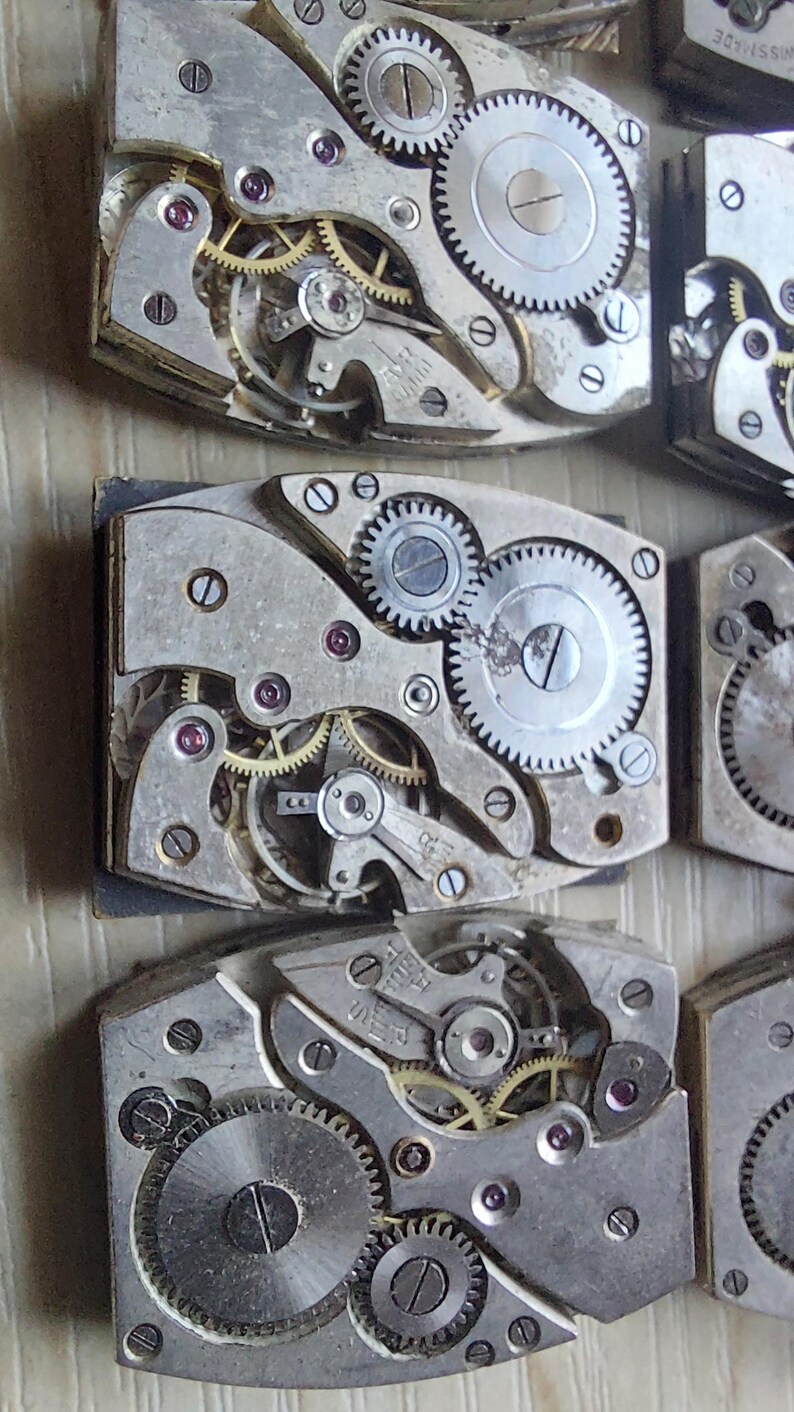 Peut inclure: Gros plan de plusieurs mouvements de montre vintage, pr&eacute;sentant des engrenages, des vis et des bijoux en rubis complexes. Les composants m&eacute;talliques argent&eacute;s sont dispos&eacute;s en formes rectangulaires, soulignant la pr&eacute;cision de l'horlogerie.