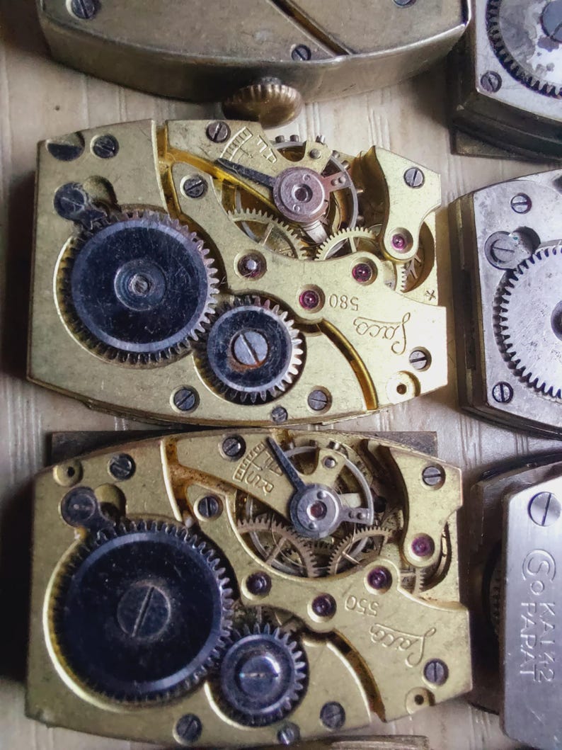 Puede incluir: Primer plano de movimientos de relojes antiguos con intrincados engranajes, tornillos y joyas. Los componentes met&aacute;licos dorados presentan la marca "Jaco" y los n&uacute;meros "580" y "550". La imagen muestra la detallada mec&aacute;nica de los relojes antiguos.