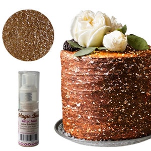 May include: A small bottle of edible gold spray for cakes and desserts. The bottle is labeled "Magic Dust Aztec Gold Edible Food Grade Made from gum Arabic Based Pearlescent and colorants www.ohsweettart.com". The spray is shown on a cake decorated with edible gold flakes.