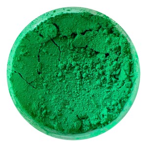 May include: A close-up view of a small, round container filled with a bright green powder. The powder has a slightly textured surface and appears to be finely ground.