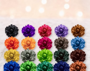 Könnte beinhalten: Eine Sammlung von zwanzig einzelnen blumenförmigen Verzierungen, die in einem Raster angeordnet sind. Jedes Stück zeigt geschichtete, gerüschte Blütenblätter in einer Vielzahl von Volltonfarben, darunter Schwarz, Lila, Pink, Orange, Gelb, Grau, Grün, Blau und Braun.