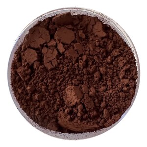 May include: A close-up view of a brown powder in a clear glass container. The powder is finely ground and has a smooth texture.