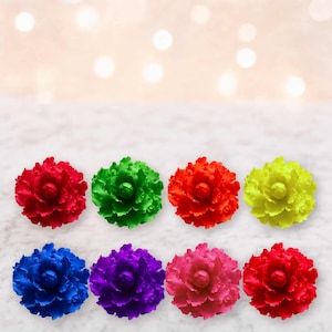 May include: A set of eight flower-shaped ornaments arranged in two rows. The colors include red, green, orange, yellow, blue, purple, pink, and a darker red. Each piece features layered, ruffled petals radiating from a central point.