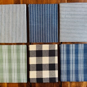 May include: Six rectangular fabric-covered notebooks arranged in two rows. The top row features vertical blue and white stripes, solid blue with white pinstripes, and horizontal blue and white stripes. The bottom row shows green plaid, black and white buffalo check, and blue plaid patterns.
