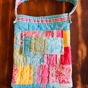 May include: A quilted patchwork shoulder bag in a variety of colors, including blue, pink, yellow, and green. The bag features a long strap and is made from various fabric patterns. The bag is likely handmade.