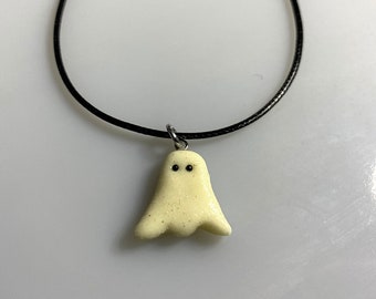 May include: A white ghost charm necklace with black eyes on a black cord.