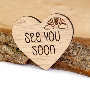 Puede incluir: Un letrero de madera en forma de corazón con un diseño de arcoíris y nubes en la parte superior y el texto "See You Soon" en una fuente manuscrita.