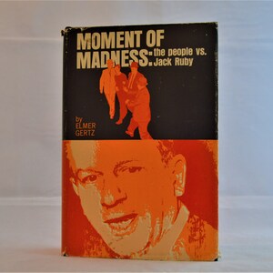 May include: Vintage book titled "Moment of Madness" by Elmer Gertz. The cover features a black background with orange figures and text. The bottom half of the cover has an orange portrait of a man.
