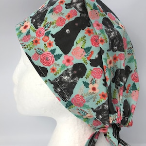 May include: A light blue scrub cap with a repeating pattern of black dogs and pink, orange, and white flowers. The cap has a tie closure at the back and is made of a soft fabric.