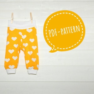 Puede incluir: Un patrón PDF para coser pantalones de bebé amarillos con corazones blancos. Los pantalones están colgados en una cuerda para la ropa con pinzas.