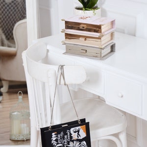 May include: A black clutch bag with a silver chain strap. The bag is decorated with an embroidered image of a book cover with the title "Dante's Divine Comedy".