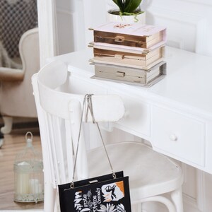 May include: A black clutch bag with a silver chain strap. The bag is decorated with an embroidered image of a book cover with the title "Dante's Divine Comedy".