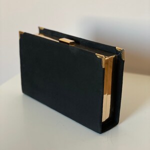May include: A black velvet clutch with gold metal accents and a clasp.