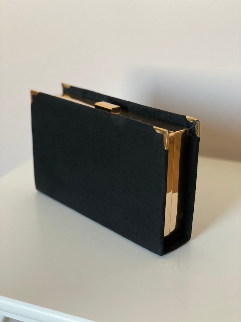 May include: A black velvet clutch with gold metal accents and a clasp.