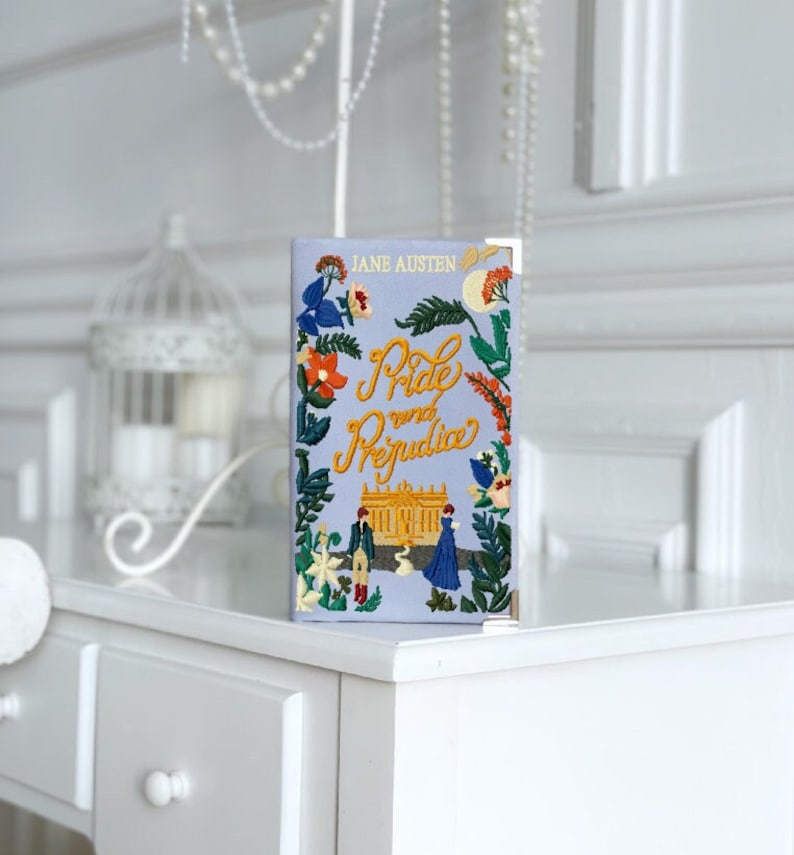 May include: A blue book with a floral design and the title "Pride and Prejudice" by Jane Austen. The book features a small illustration of a couple in front of a building.