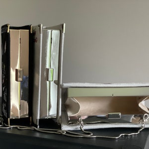 May include: Three silver clutch purses with chain straps. One is black with white embroidery, one is gray, and one is open to show the interior lining.
