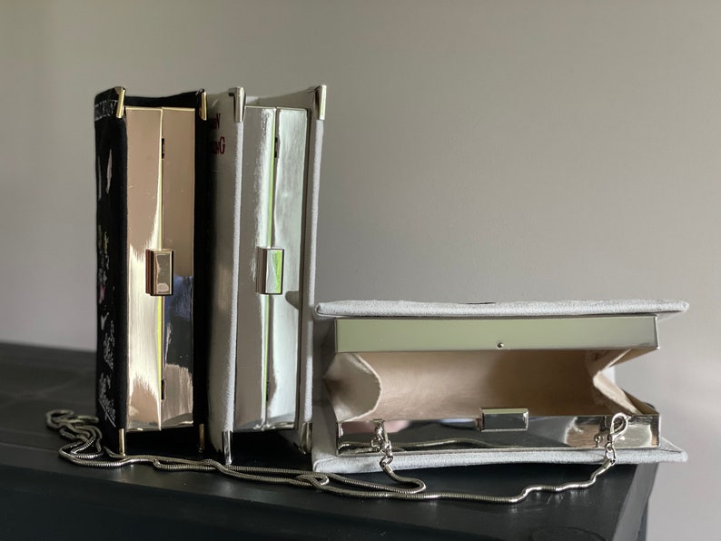 May include: Three silver clutch purses with chain straps. One is black with white embroidery, one is gray, and one is open to show the interior lining.