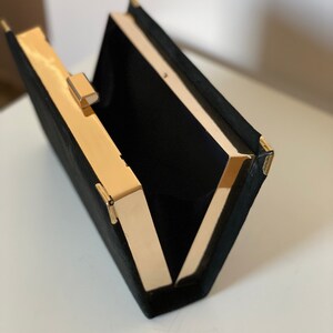 May include: A black velvet clutch with a gold metal frame and clasp. The clutch is open and the interior is lined with black fabric.