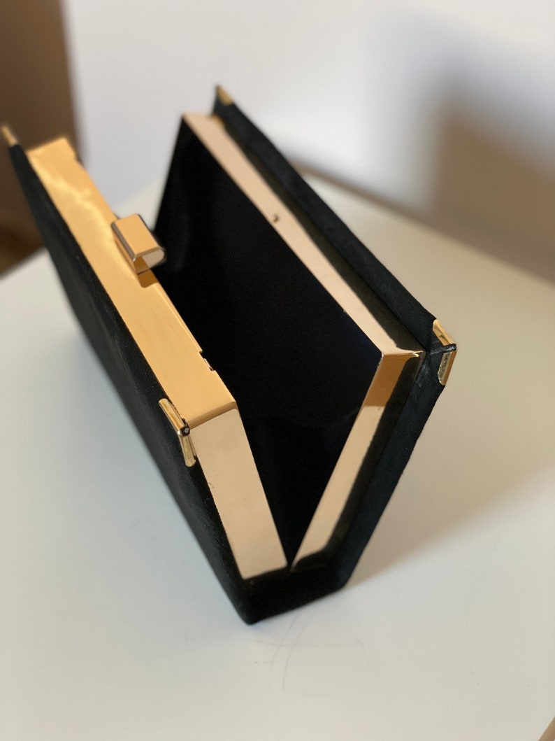May include: A black velvet clutch with a gold metal frame and clasp. The clutch is open and the interior is lined with black fabric.