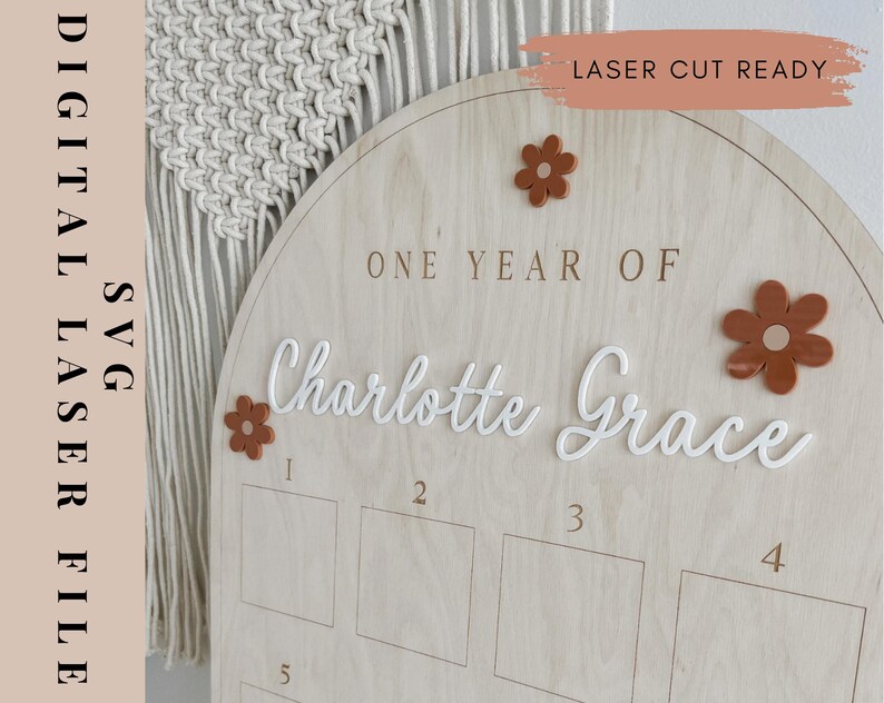 May include: A wooden sign with a rounded top, featuring the text "One Year Of Charlotte Grace" in white cursive lettering. The sign has five numbered squares for recording milestones, and is decorated with brown flower cutouts.
