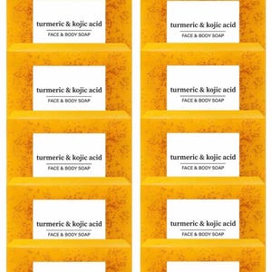Op de afbeelding: Een stapel gezichts- en lichaamszeep met kurkuma en kojiczuur. Elke zeep is een levendige gele kleur met een getextureerd oppervlak. Witte labels met zwarte tekst lezen "turmeric & kojic acid FACE & BODY SOAP".