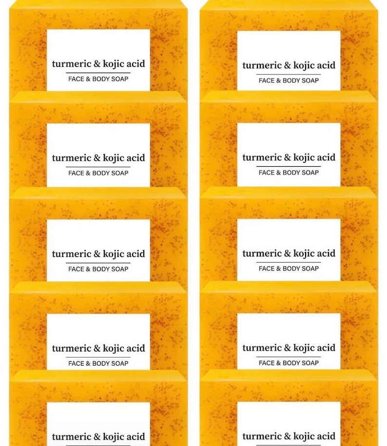 Op de afbeelding: Een stapel gezichts- en lichaamszeep met kurkuma en kojiczuur. Elke zeep is een levendige gele kleur met een getextureerd oppervlak. Witte labels met zwarte tekst lezen "turmeric & kojic acid FACE & BODY SOAP".