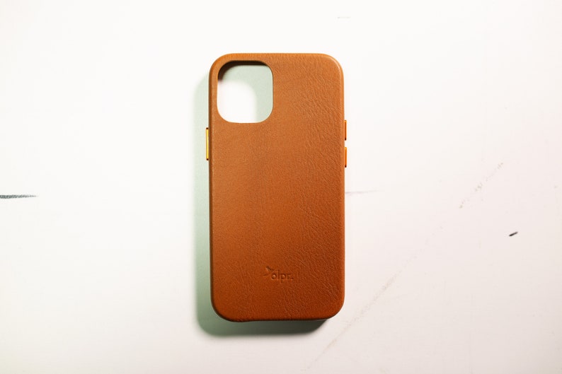May include: A brown leather phone case with a gold trim and the word "alpa" embossed on the back.