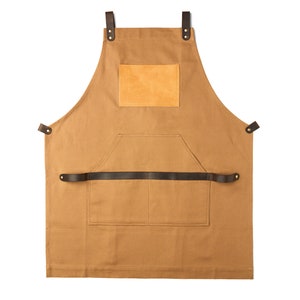 May include: A brown canvas apron with leather straps and a brown leather patch pocket. The apron has a large front pocket and a smaller pocket on the chest.