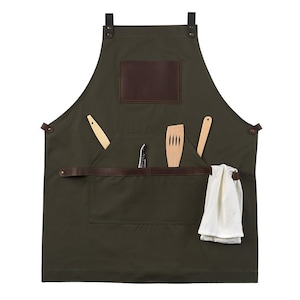 May include: A green canvas apron with brown leather straps and a large pocket. The pocket has a brown leather flap and is filled with a wooden spatula, a wooden spoon, and a small knife.