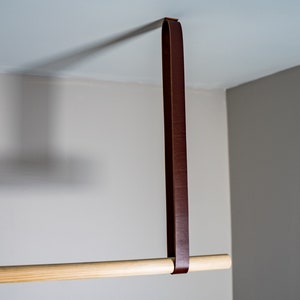 K&ouml;nnte beinhalten: Eine Holzstange mit einem braunen Lederriemen, der von der Decke h&auml;ngt. Der Riemen ist mit einer Schlaufe an der Stange befestigt.
