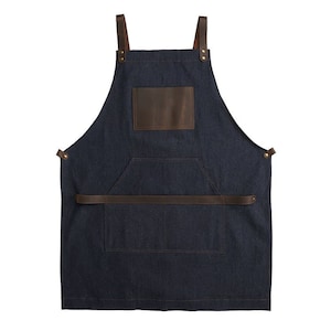 May include: A dark blue denim apron with brown leather straps and a large brown leather pocket. The apron has a single large pocket on the front and a smaller pocket on the chest.