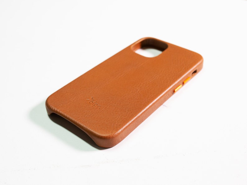 May include: A brown leather phone case with a raised "dbrand" logo. The case has a cutout for the camera lens and a raised lip around the edges.
