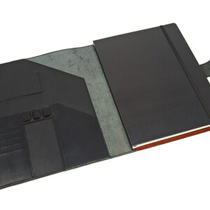 May include: A black leather notebook with a built-in elastic closure and a flap with multiple pockets and card slots. The notebook is open to reveal a blank page.