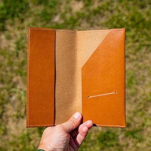 May include: A brown leather wallet with a fold-over flap and a single pocket on the inside. The wallet is open and the inside is visible.