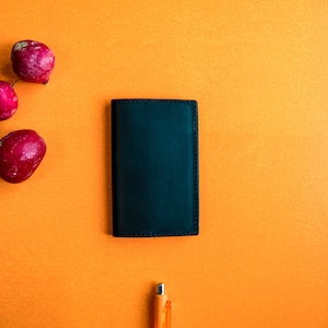 May include: A black leather wallet on a bright orange surface with three red radishes.