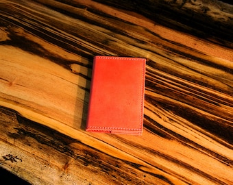May include: A red leather notebook with stitched edges, lying on a wooden surface.