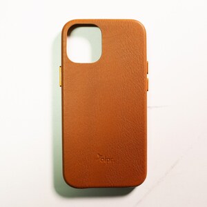 May include: A brown leather phone case with a gold accent around the camera lens and volume buttons. The case has the word "dbrand" embossed on the back.