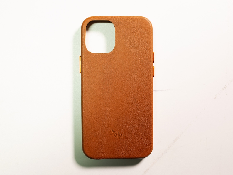 May include: A brown leather phone case with a gold accent around the camera lens and volume buttons. The case has the word "dbrand" embossed on the back.