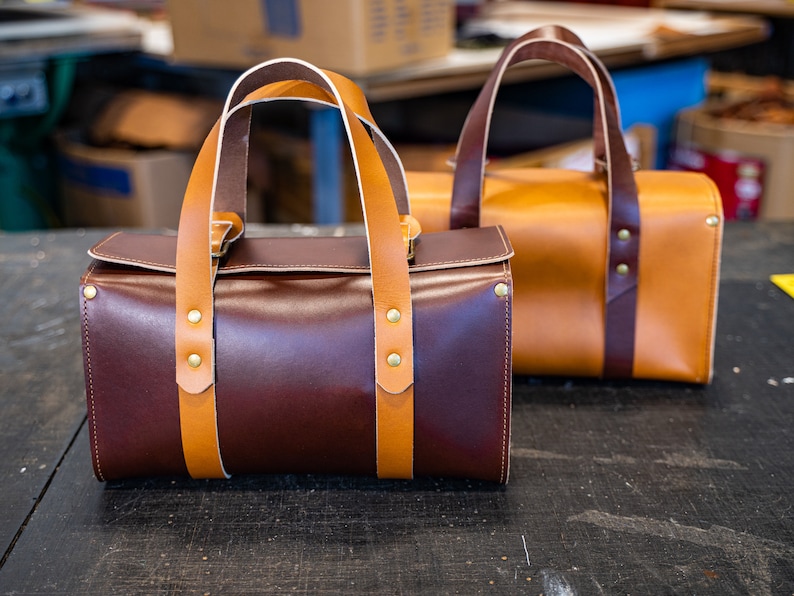 K&ouml;nnte beinhalten: Zwei Ledertaschen mit braunen und hellbraunen Lederriemen. Die Tasche links ist dunkelbraun und die Tasche rechts ist hellbraun.