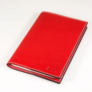 May include: A red leather notebook with white stitching and the initials "A.T." embossed on the front.