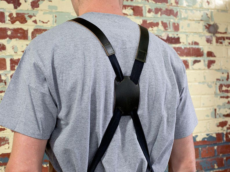 May include: A person wearing a gray t-shirt with black suspenders. The suspenders have a leather strap and a black buckle.