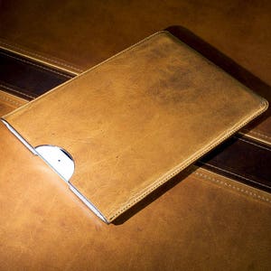 May include: A brown leather case for a tablet or laptop computer. The case is closed and has a flap that folds over the front.