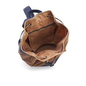 May include: A brown canvas drawstring backpack with a blue canvas bottom. The backpack is open and empty, showing the inside of the bag.