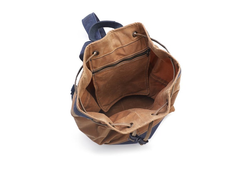 May include: A brown canvas drawstring backpack with a blue canvas bottom. The backpack is open and empty, showing the inside of the bag.